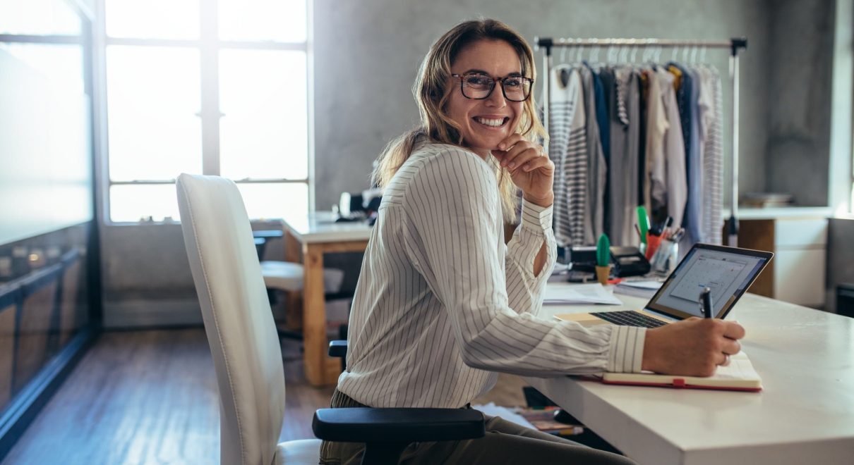 blond woman glasses sitting desk laptop pen diary clothing rack.jpg